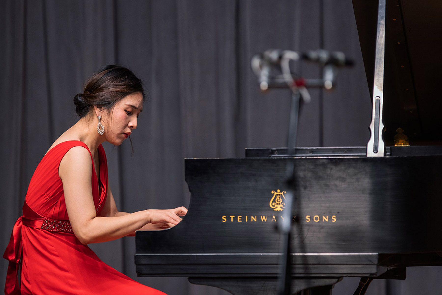 Pianist in vibrant red dress performs on a black Steinway grand piano, focused and elegant against a dark backdrop.