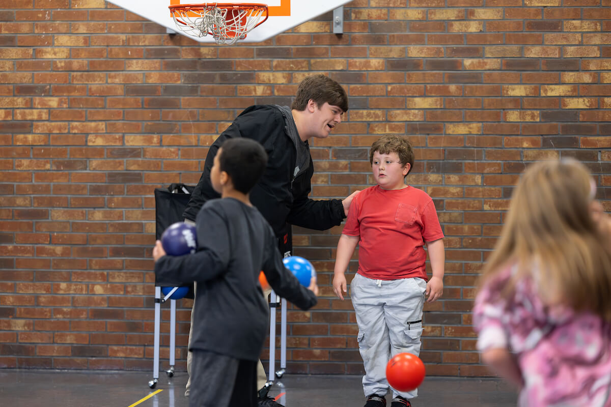 A student teacher talks to an elementary school student during a physical education activity